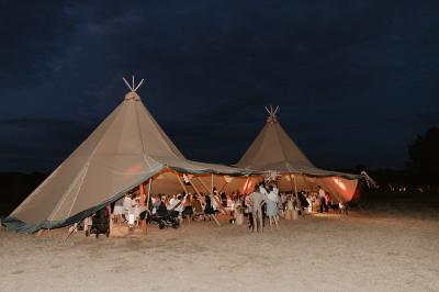 Fête nocturne en plein air avec un bar central, des invités debout et des lumières colorées sous une tente éclairée.