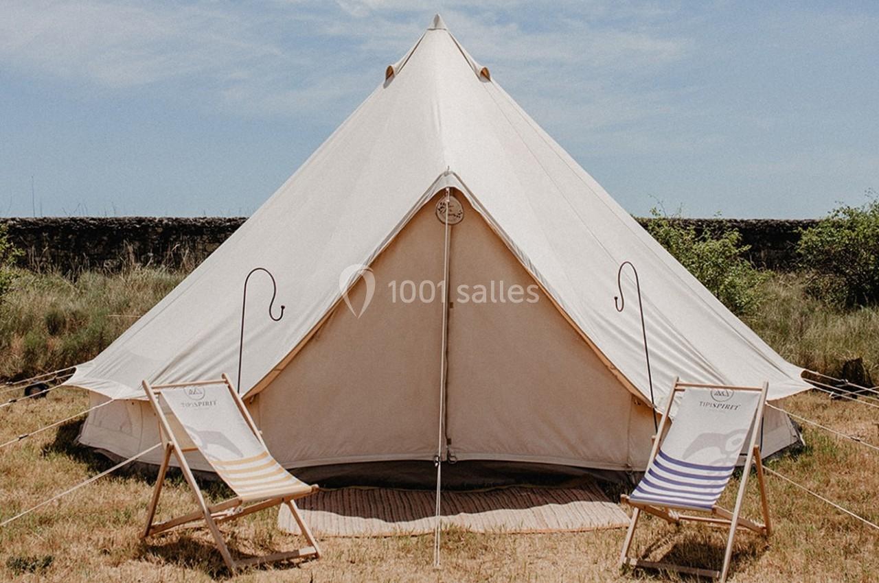 Tente blanche en toile installée sur une pelouse, entourée de deux chaises longues rayées.