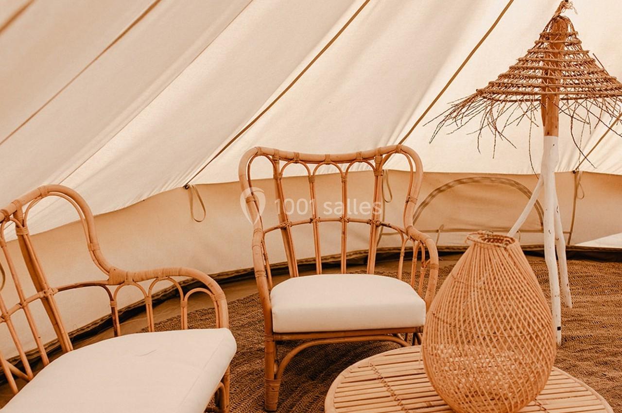 Mobilier en rotin avec coussins blancs dans une tente beige, accompagné d'une lampe et d'une table assorties.