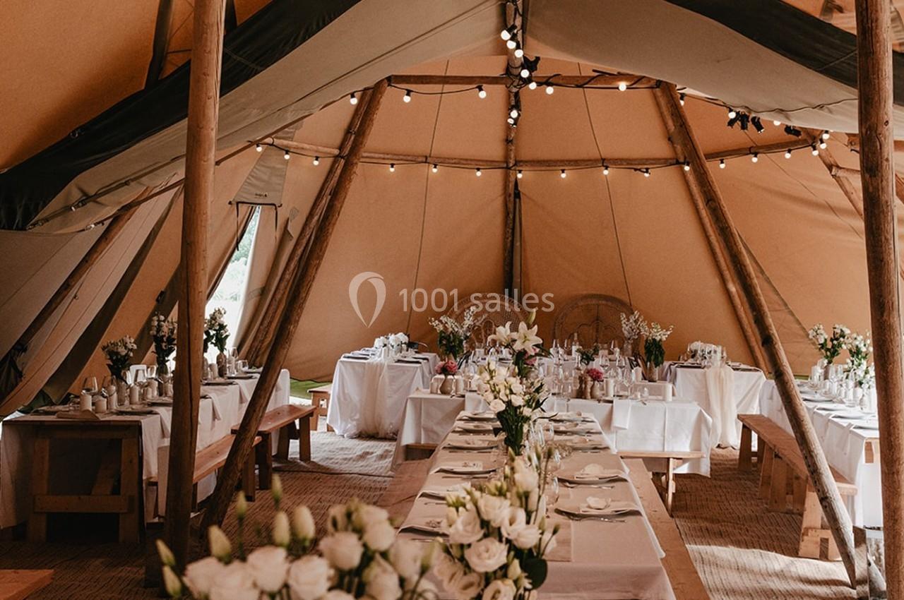 Intérieur d'une tente décorée pour un événement, avec tables dressées, nappes blanches et arrangements floraux.
