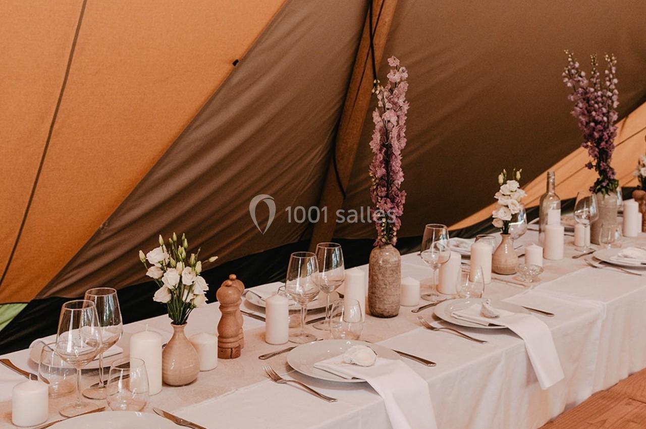 Table dressée sous une tente avec vaisselle blanche, bougies, vases de fleurs et verres disposés élégamment.
