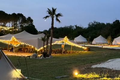 Fête nocturne en plein air avec un bar central, des invités debout et des lumières colorées sous une tente éclairée.