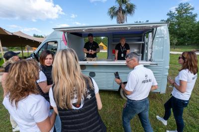 Fête nocturne en plein air avec un bar central, des invités debout et des lumières colorées sous une tente éclairée.