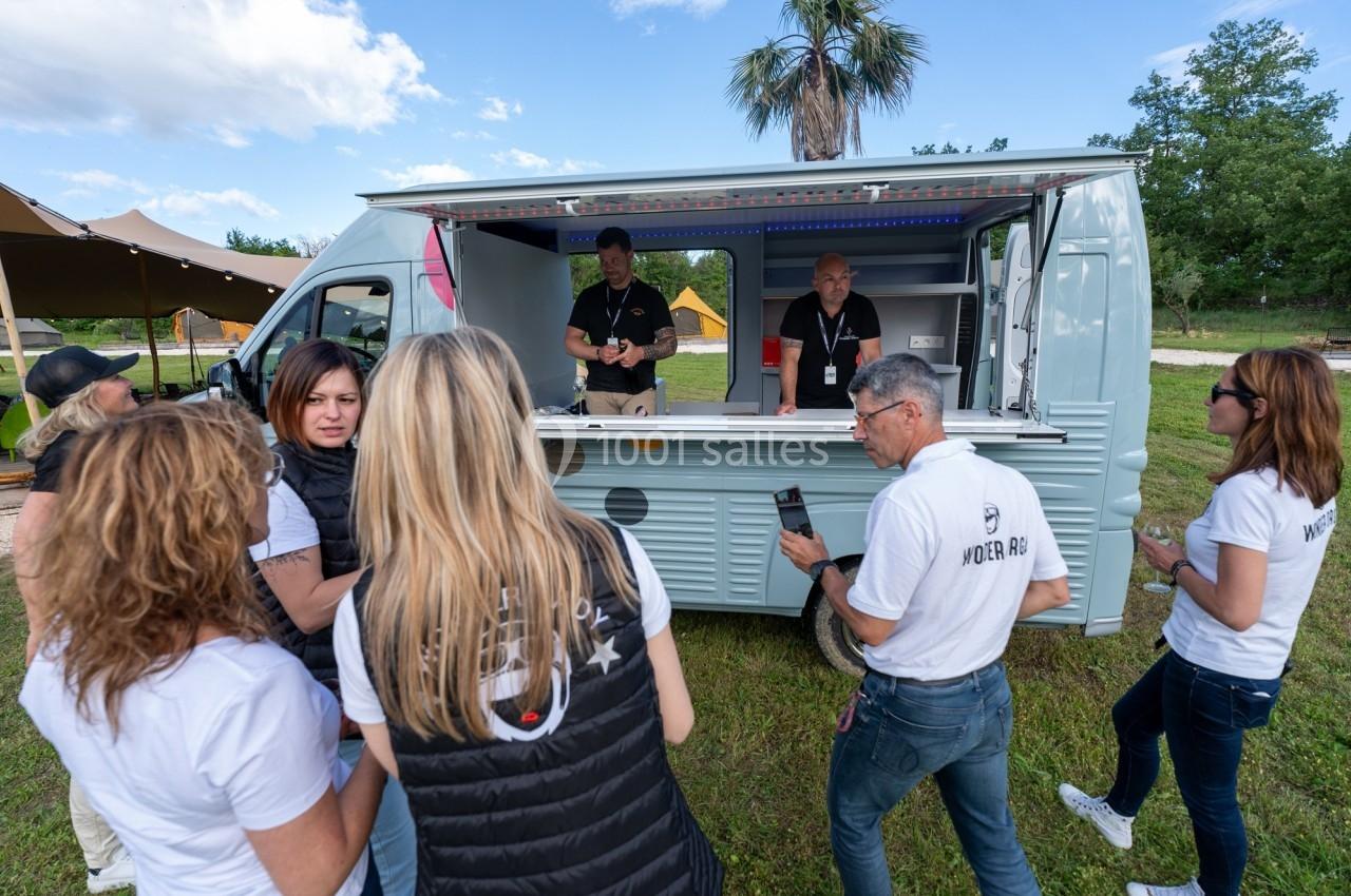 Un groupe de personnes discute devant un food truck stationné dans un espace extérieur verdoyant.