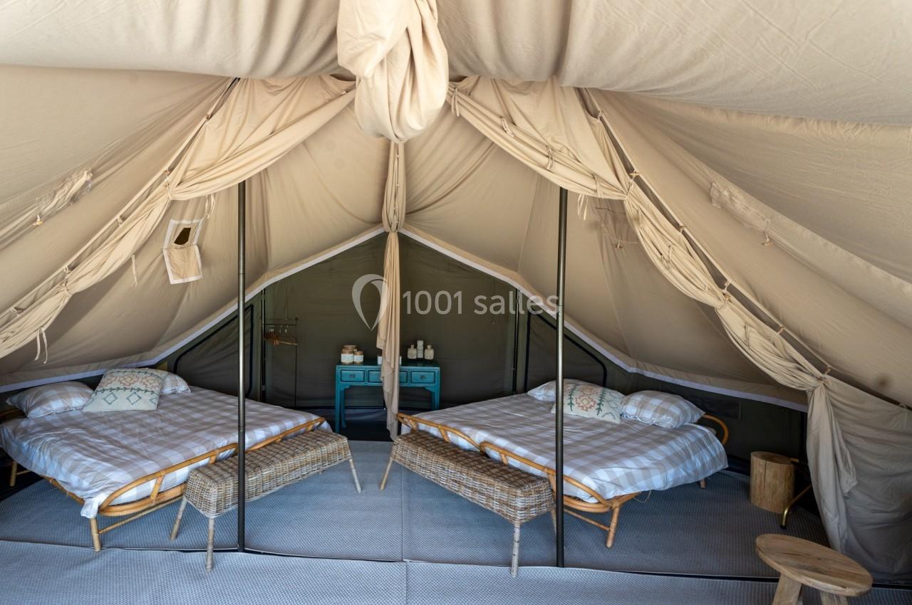 Intérieur d'une tente aménagée avec deux lits, des tables de chevet et une décoration simple et fonctionnelle.