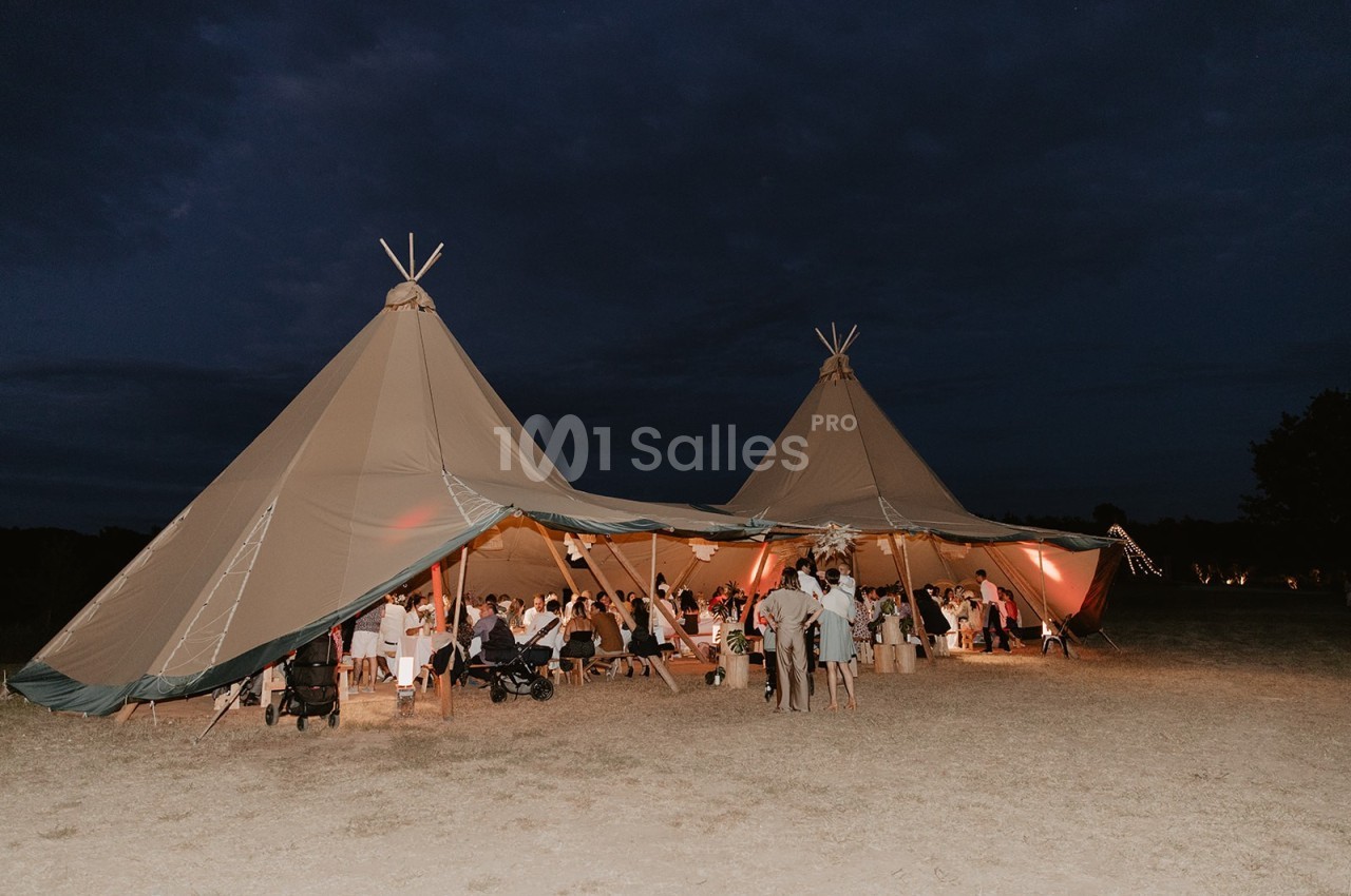 Deux grandes tentes tipi éclairées accueillent un rassemblement de personnes en soirée dans un espace extérieur.