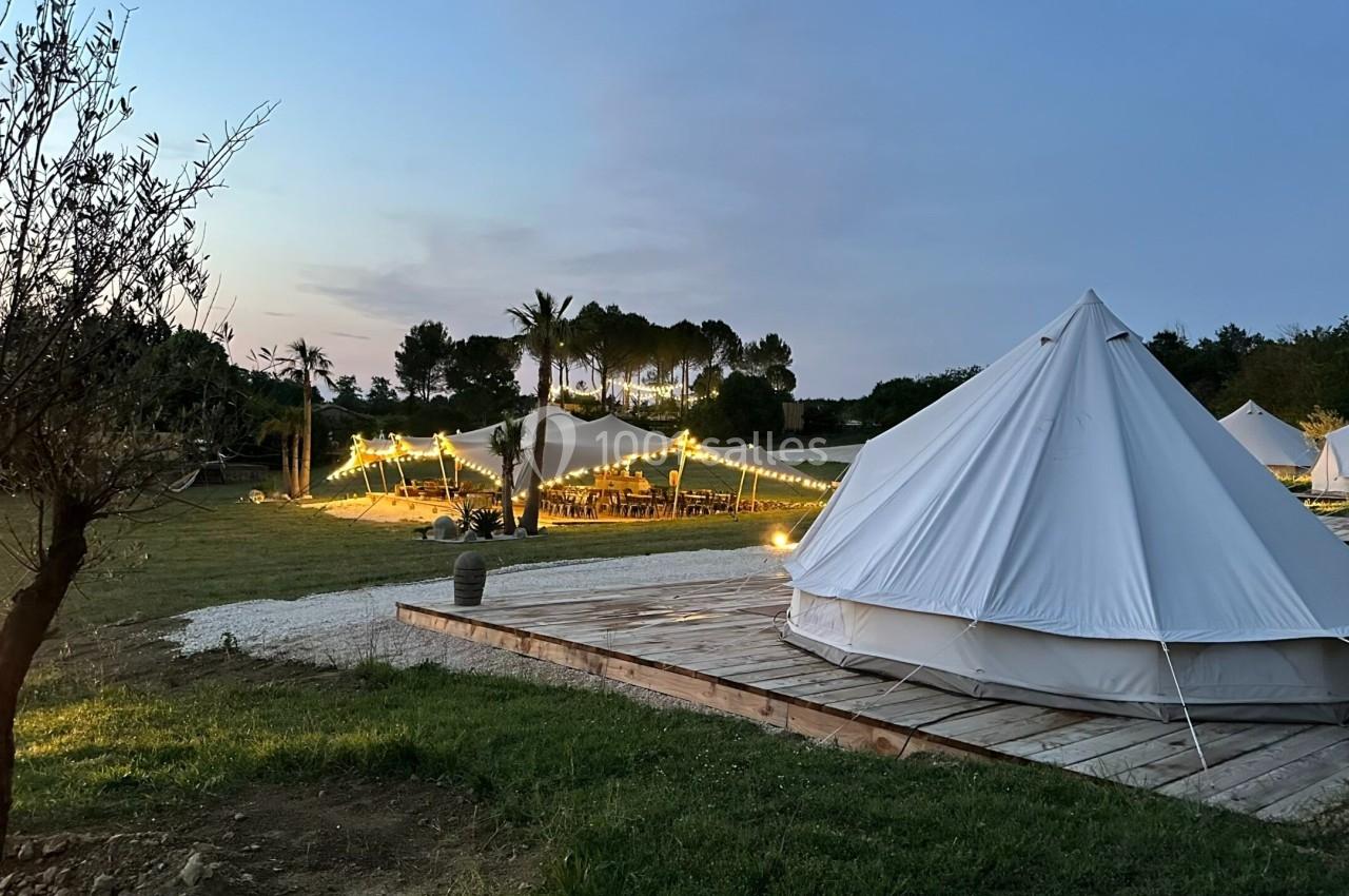 Tentes blanches installées dans un champ au crépuscule, avec des guirlandes lumineuses éclairant un espace de réception.