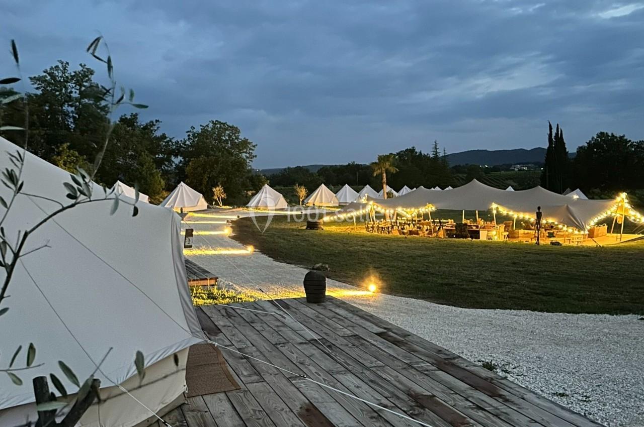 Tentes éclairées par des guirlandes lumineuses dans un cadre naturel au crépuscule.