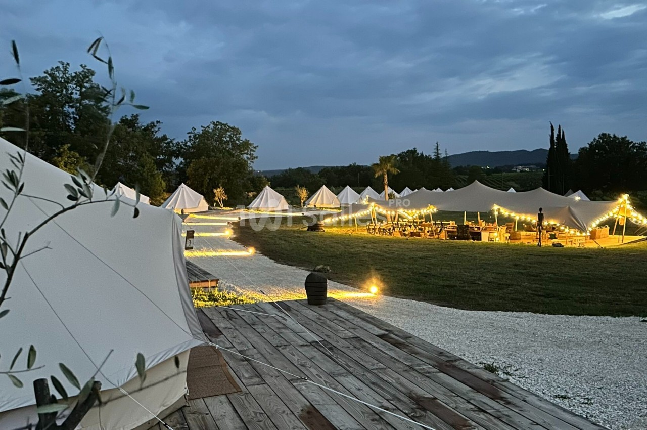 Tentes éclairées par des guirlandes lumineuses dans un cadre naturel au crépuscule.