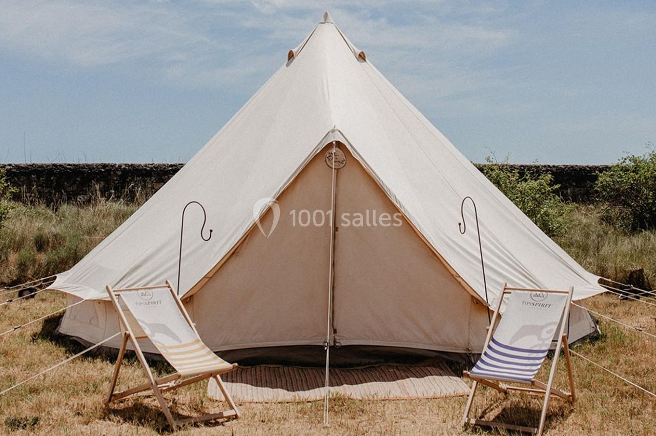 Tente en toile beige montée sur un terrain herbeux, entourée de deux chaises longues rayées.