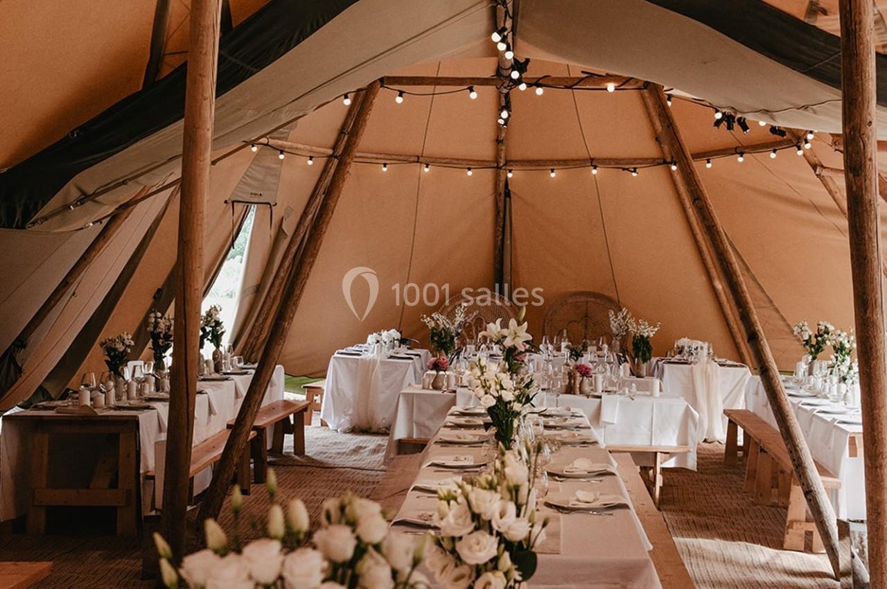 Intérieur d'une tente décorée pour un événement, avec tables dressées, nappes blanches et arrangements floraux.