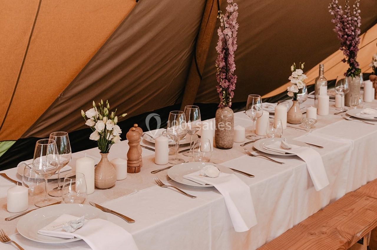 Table dressée avec nappes blanches, vaisselle élégante, bougies et fleurs dans un décor de tente.