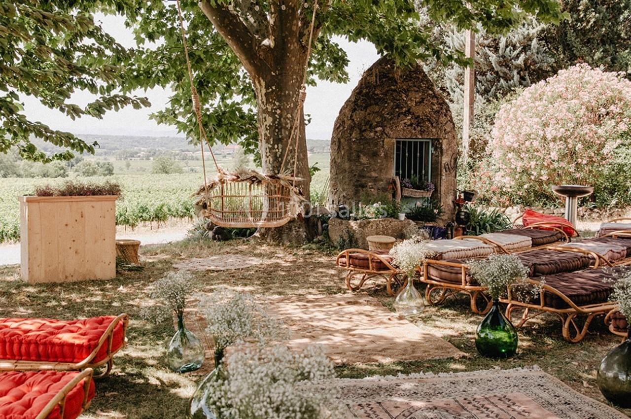 Espace extérieur aménagé avec des fauteuils en rotin, tapis, coussins et balançoire sous un arbre, près d'un paysage…