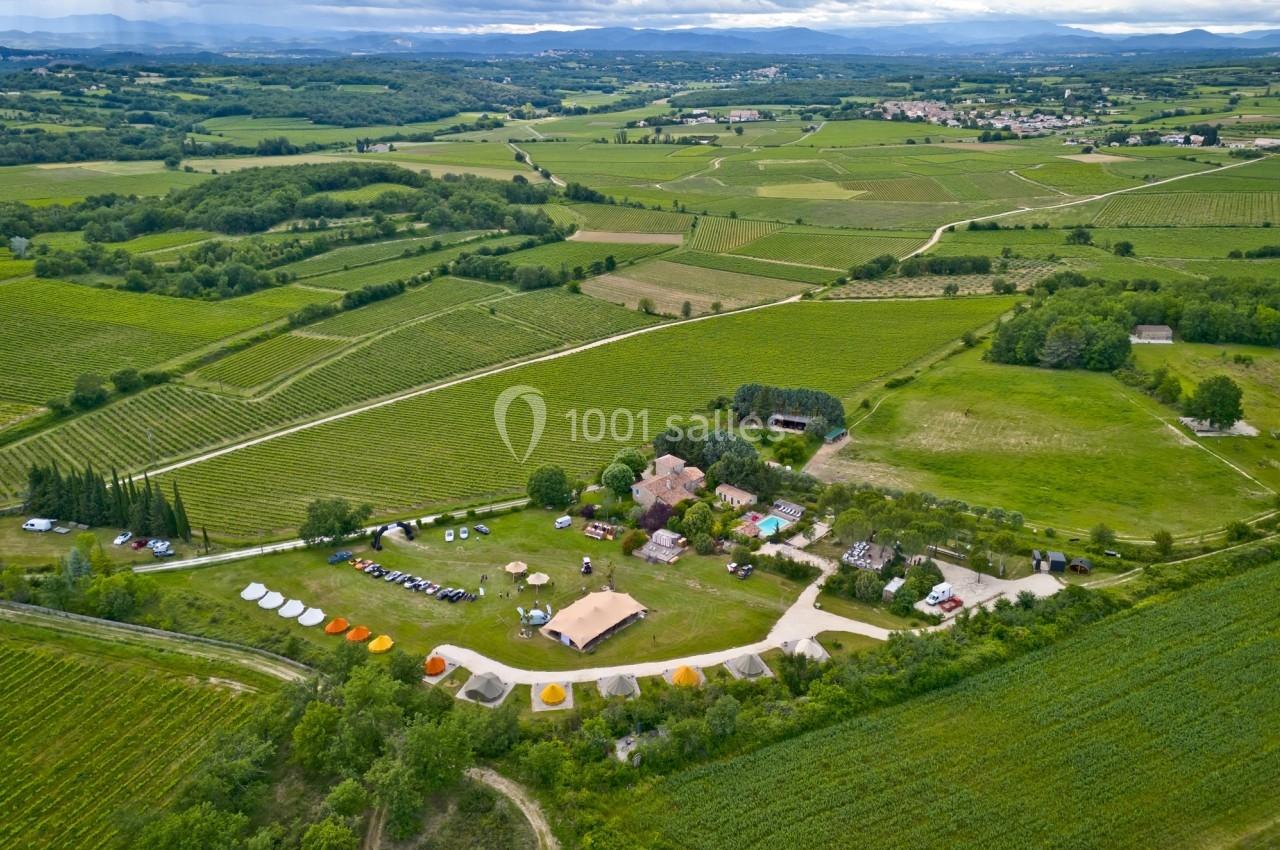 Vue aérienne d'un domaine rural avec des vignes, des bâtiments et des tentes entourés de champs verdoyants.