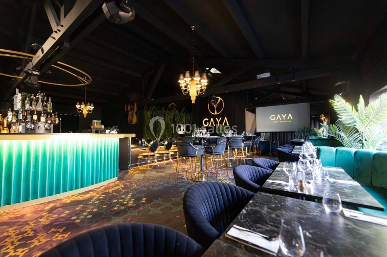 Salle de restaurant élégante avec bar lumineux, tables dressées, fauteuils bleus et décoration moderne.