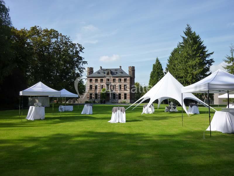Tentes blanches installées sur une pelouse devant un grand bâtiment en pierre entouré d'arbres.