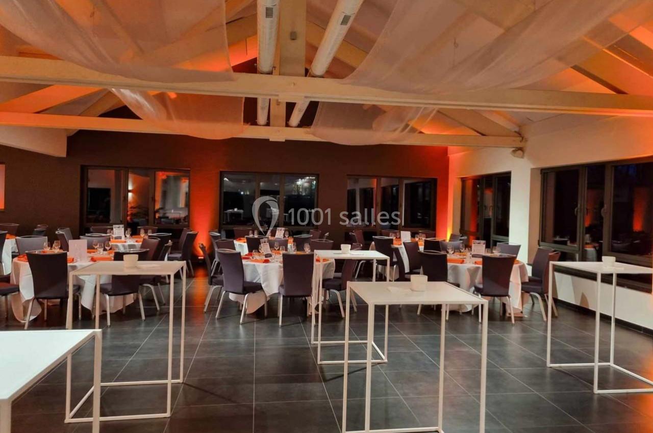 Salle de réception décorée avec des tables dressées, éclairage tamisé orange et plafond avec voilages suspendus.