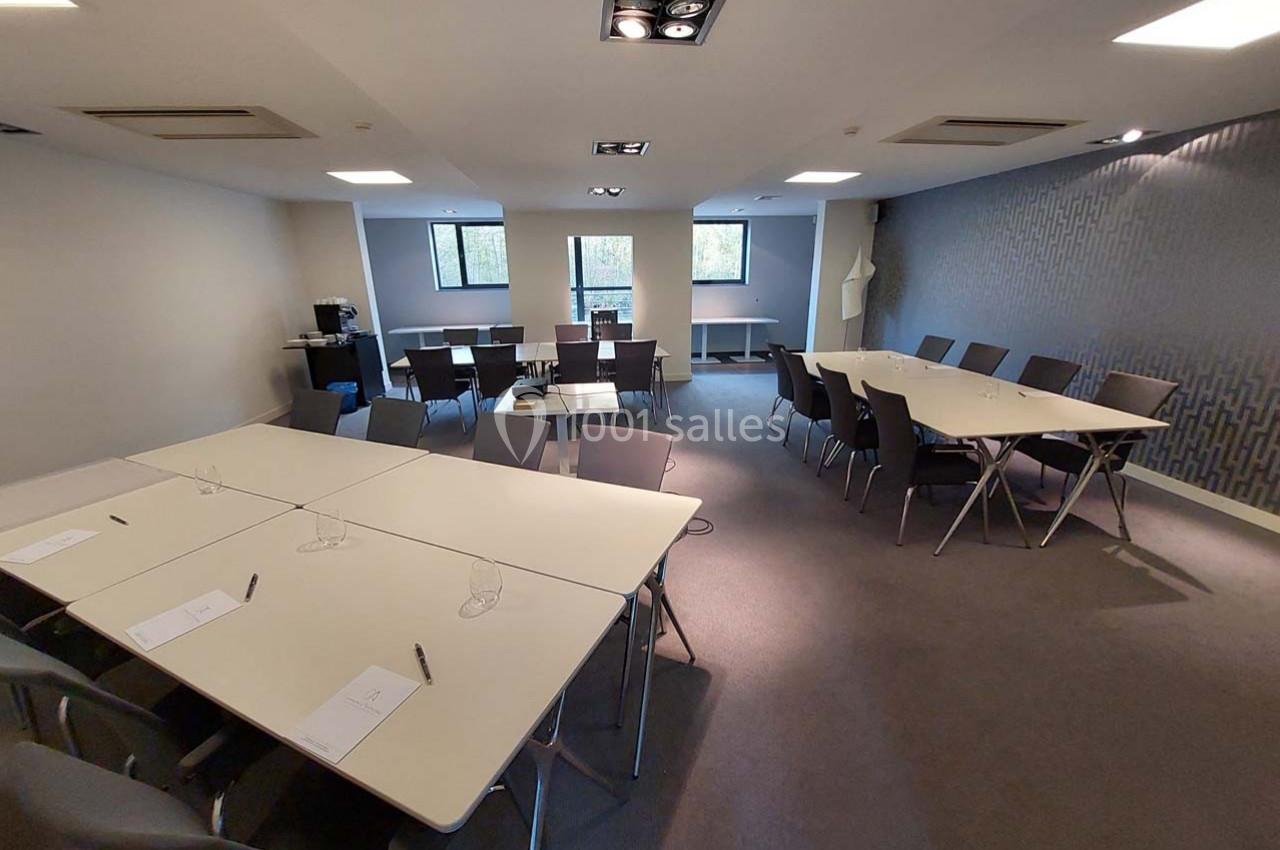 Salle de réunion lumineuse avec plusieurs tables disposées en U et en rangées, chaises et matériel de prise de notes.