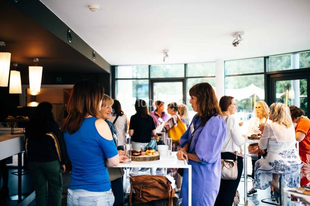 Groupe de personnes discutant autour de tables hautes dans un espace lumineux avec de grandes baies vitrées.