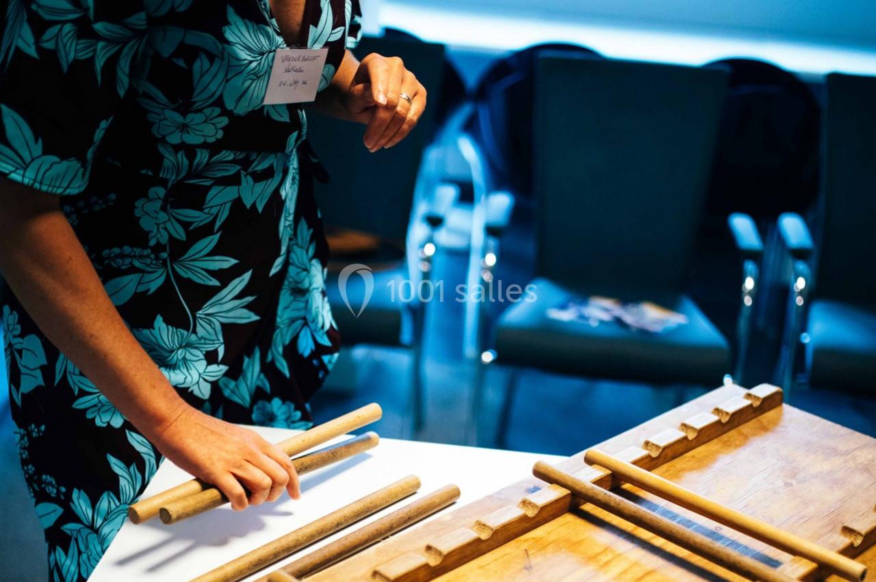 Personne manipulant des bâtons en bois sur une table, avec des chaises vides en arrière-plan.