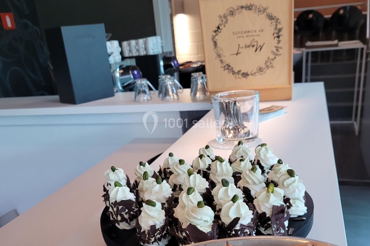 Plateau de petits desserts décorés de crème chantilly et de pistaches, posé sur un comptoir lumineux.