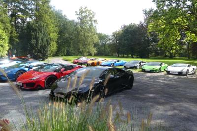 Quatre voitures sportives colorées alignées sur un parking en plein air, entourées de verdure.