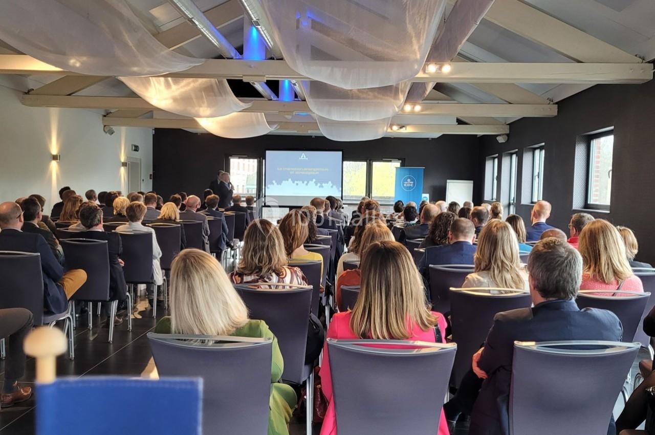 Salle de conférence avec un public assis, regardant une présentation projetée sur un écran.