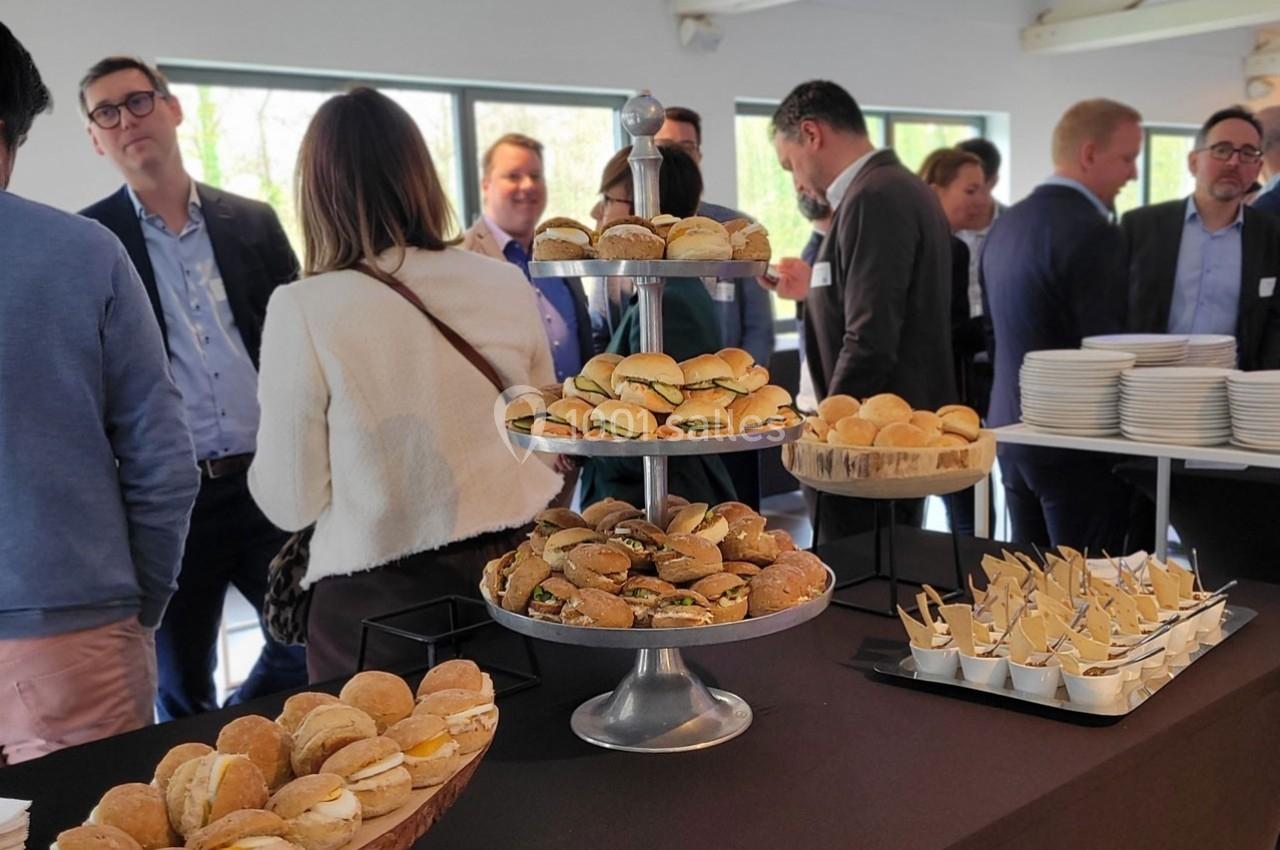 Plateau de mini-sandwichs et verrines sur une table lors d'un événement avec des participants en arrière-plan.