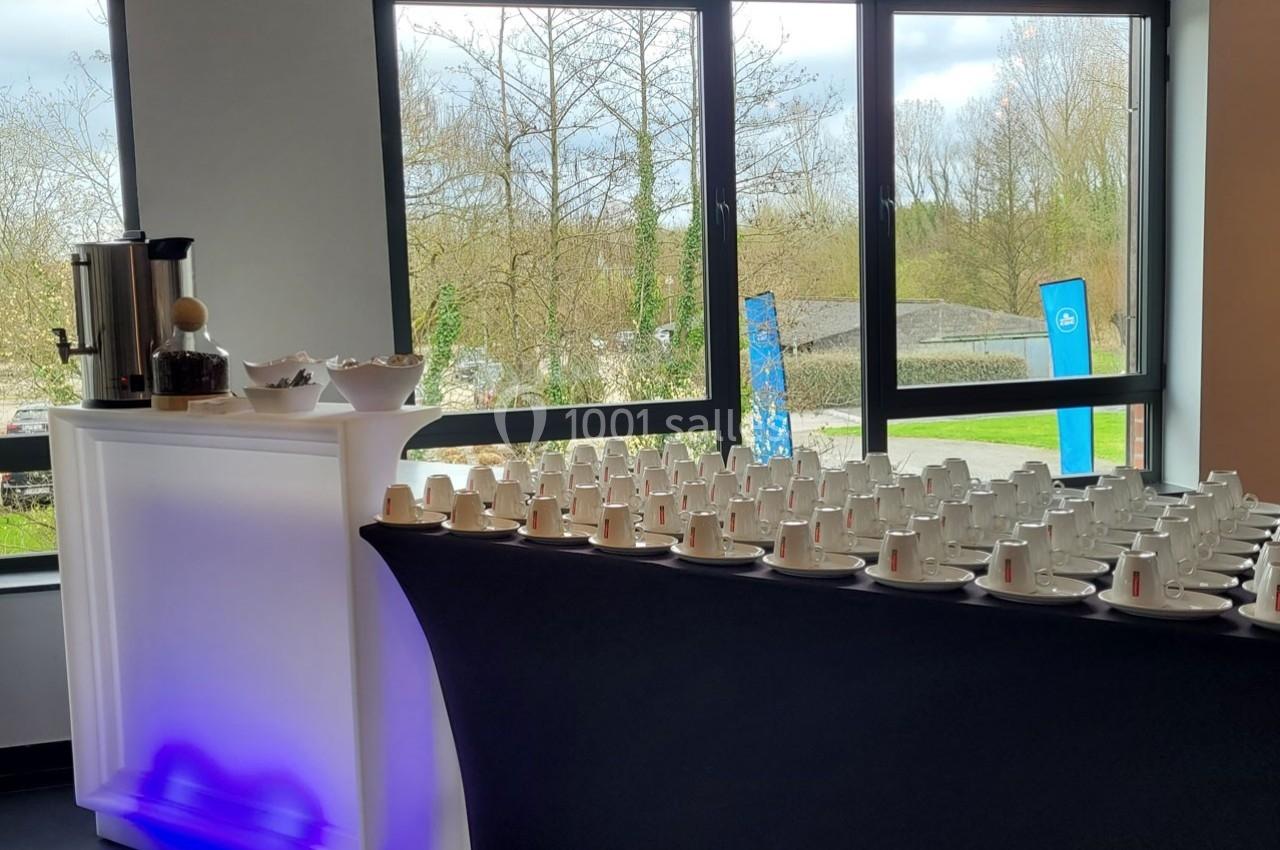 Table dressée avec des tasses empilées et une machine à café, près d'une fenêtre donnant sur un paysage extérieur.