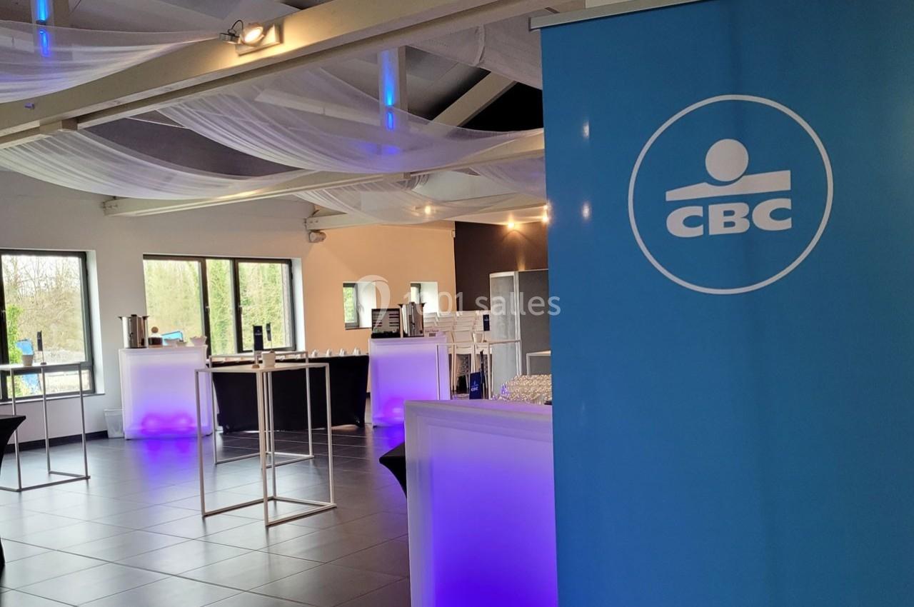 Salle lumineuse avec tables hautes, éclairage violet et un panneau bleu avec le logo ’CBC’ au premier plan.