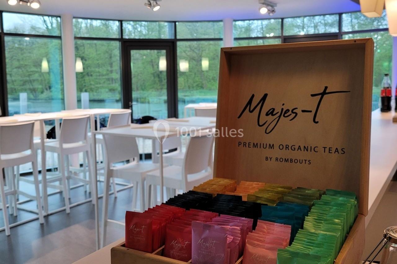 Boîte de sachets de thé colorés sur un comptoir, avec une salle lumineuse et des tables hautes en arrière-plan.