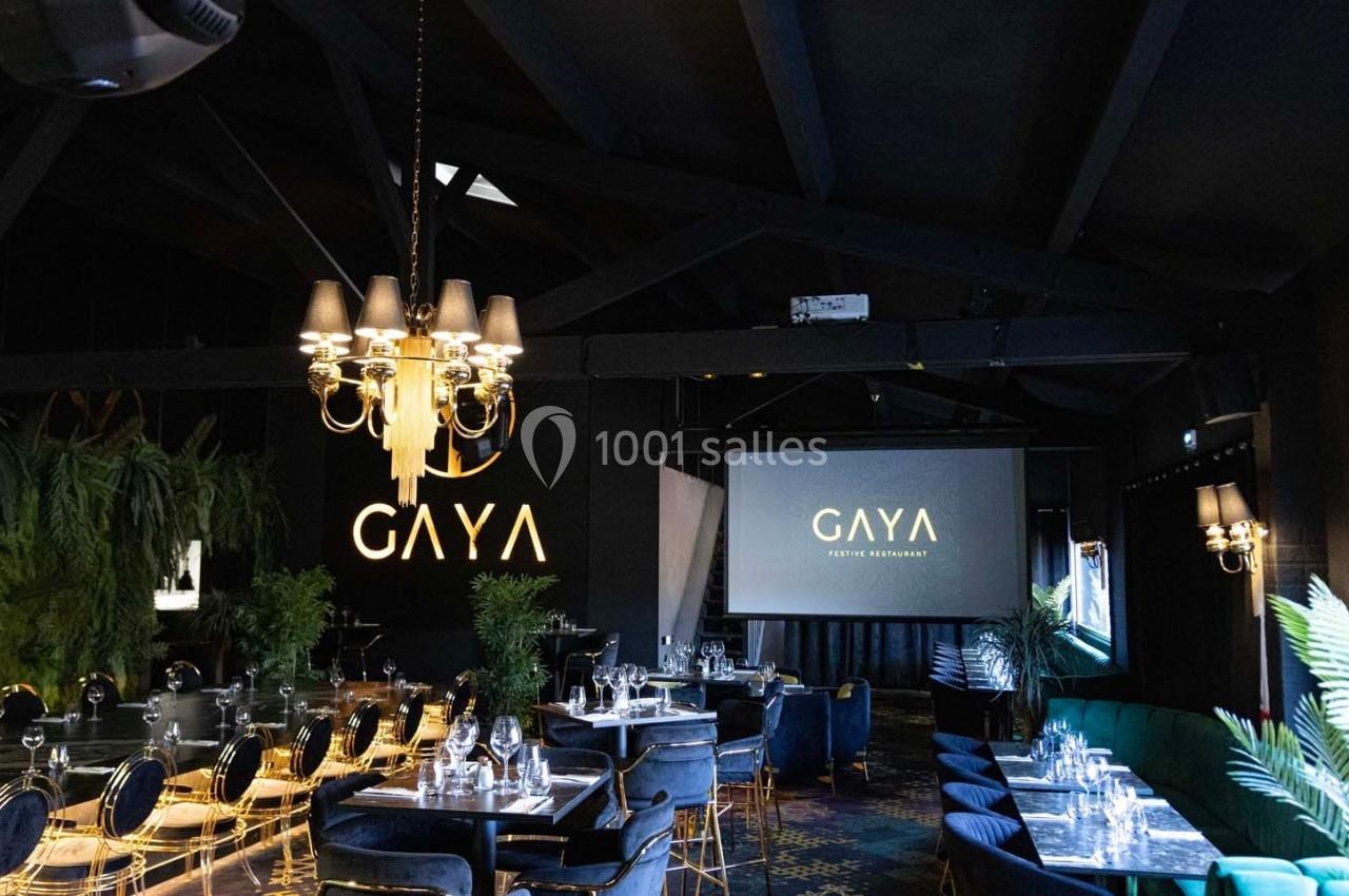 Salle de restaurant élégante avec tables dressées, décor sombre et végétation, éclairée par un grand lustre.