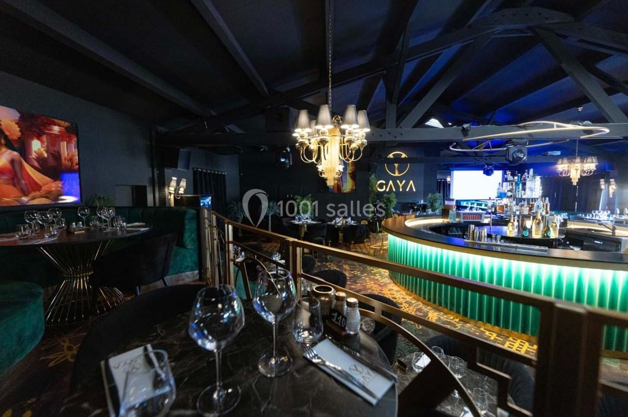 Intérieur d'un bar-restaurant élégant avec tables dressées, bar éclairé et ambiance tamisée.