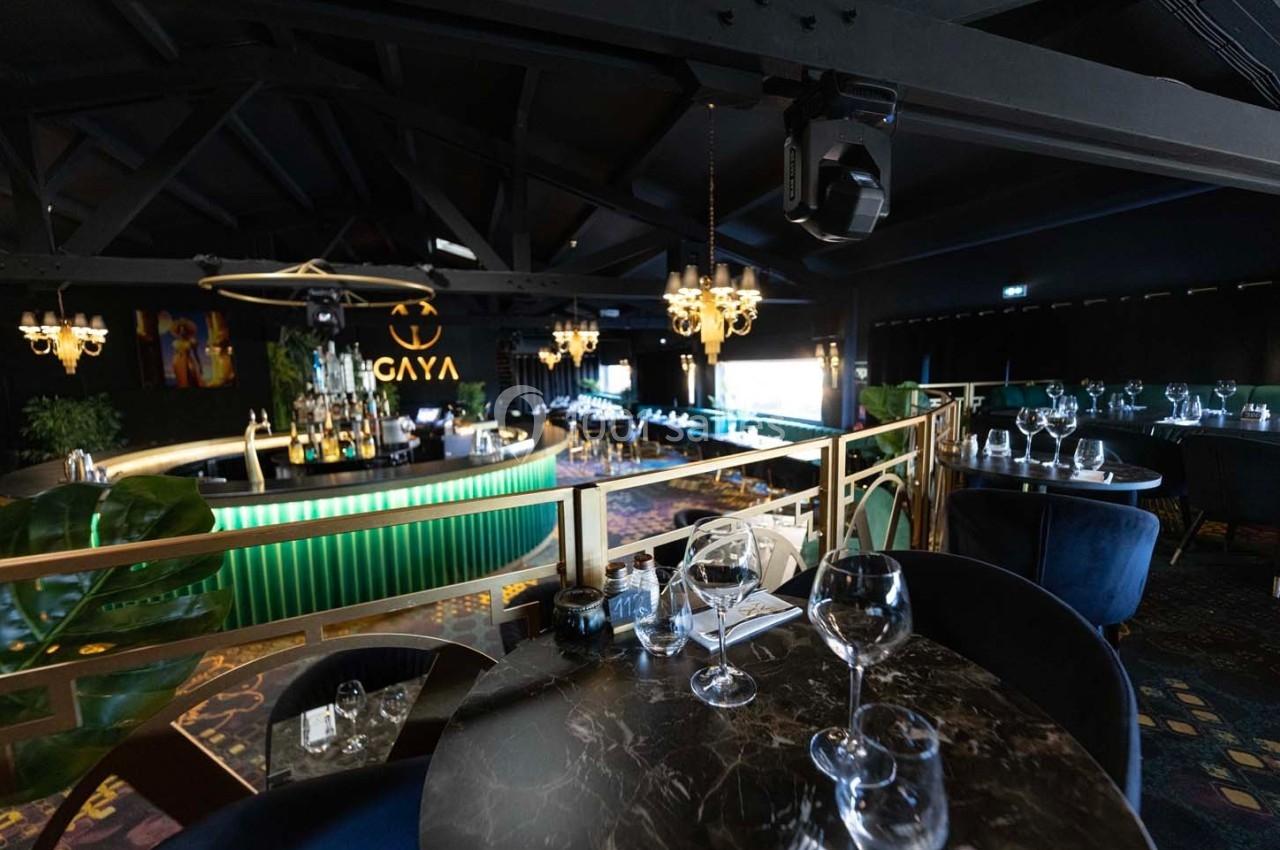 Salle de restaurant élégante avec tables dressées, bar lumineux vert et lustres suspendus dans une ambiance tamisée.