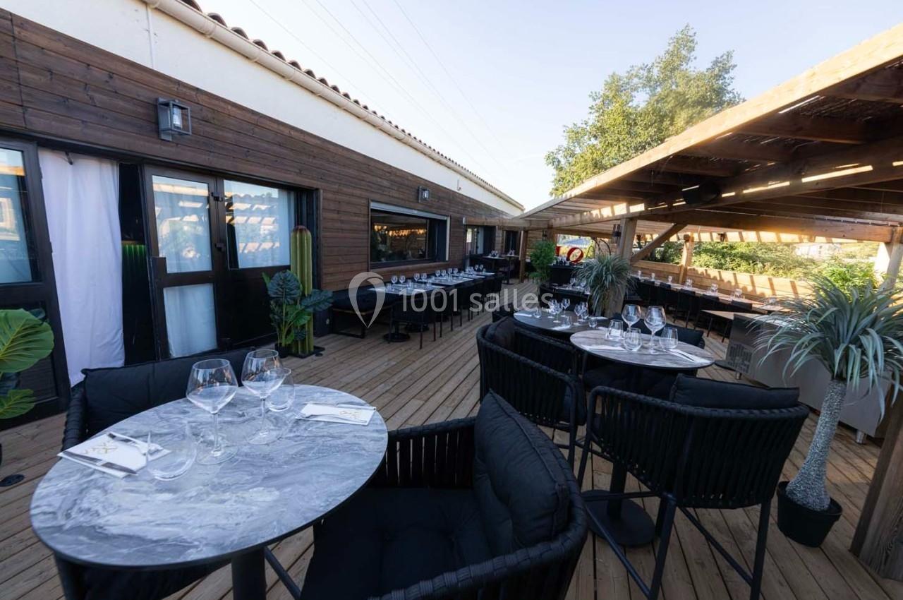 Terrasse en bois aménagée avec tables, chaises et plantes, partiellement couverte par une pergola en bois.