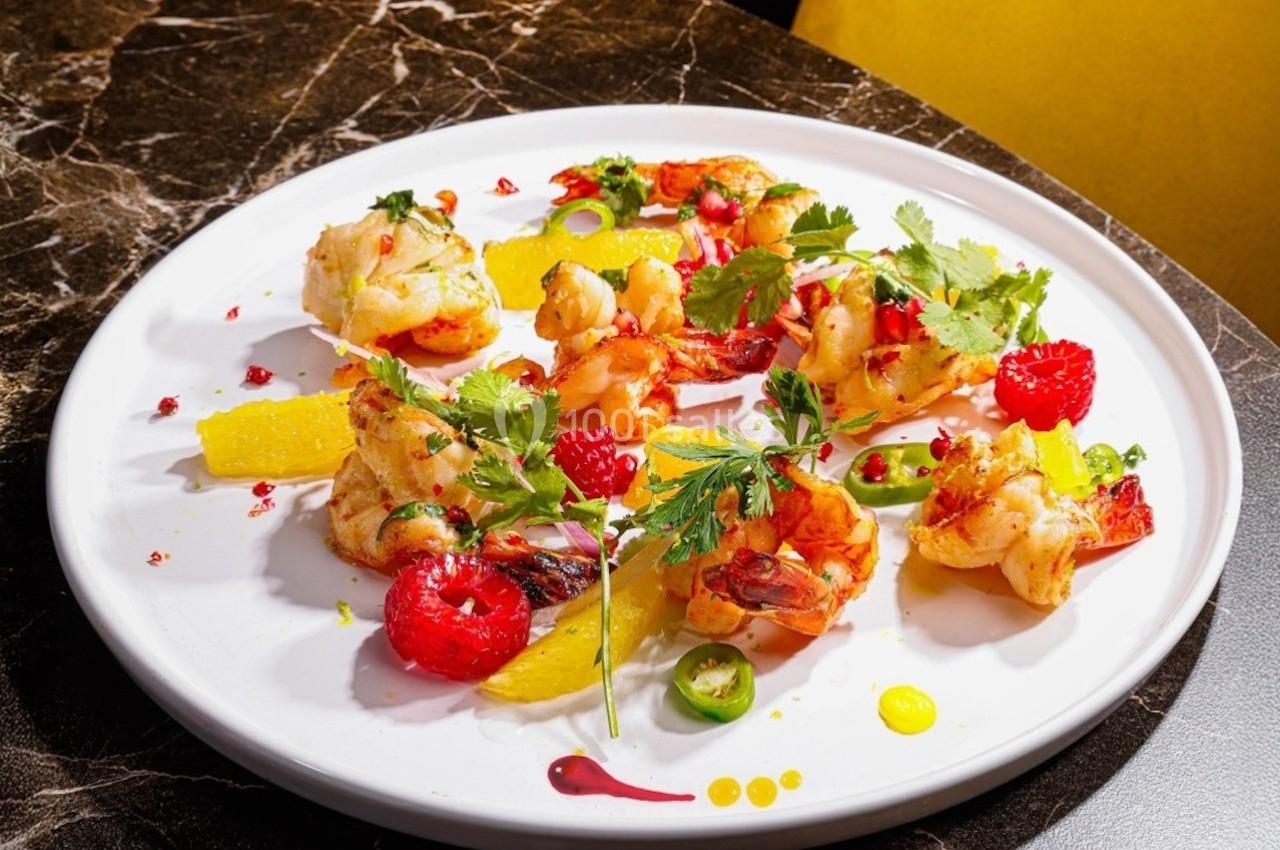 Assiette de crevettes grillées garnies de framboises, tranches d'orange, herbes fraîches et sauces colorées.