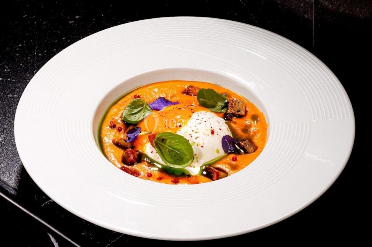 Assiette de soupe orange garnie d'un œuf poché, de basilic frais, de légumes et de pétales comestibles.
