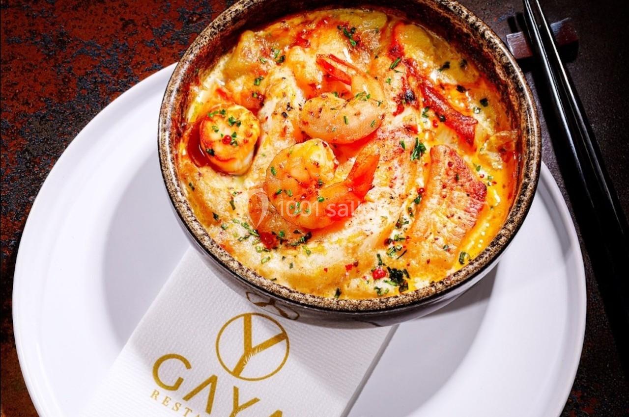 Plat de crevettes et légumes dans une sauce crémeuse, servi dans un bol en céramique sur une assiette blanche.