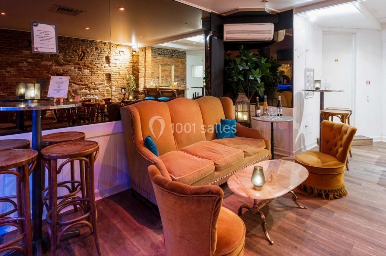 Salon chaleureux avec canapé orange, fauteuils assortis, table basse et murs en briques dans un espace lumineux.