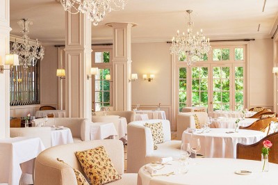 Salle de réception lumineuse avec tables décorées, chaises blanches et un grand lustre central sous une verrière.