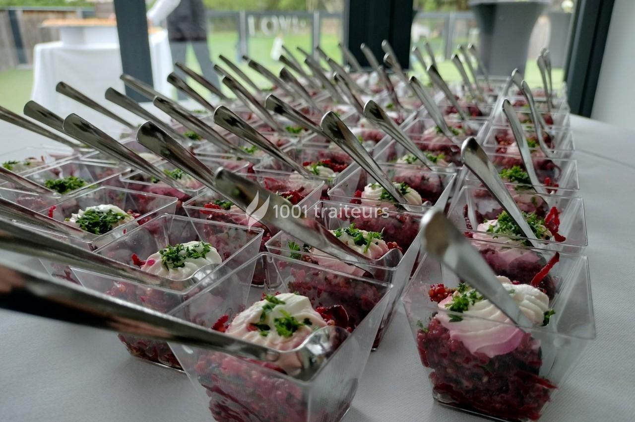 Petites verrines de betterave garnies de crème et de persil, disposées en rangées sur une table blanche.