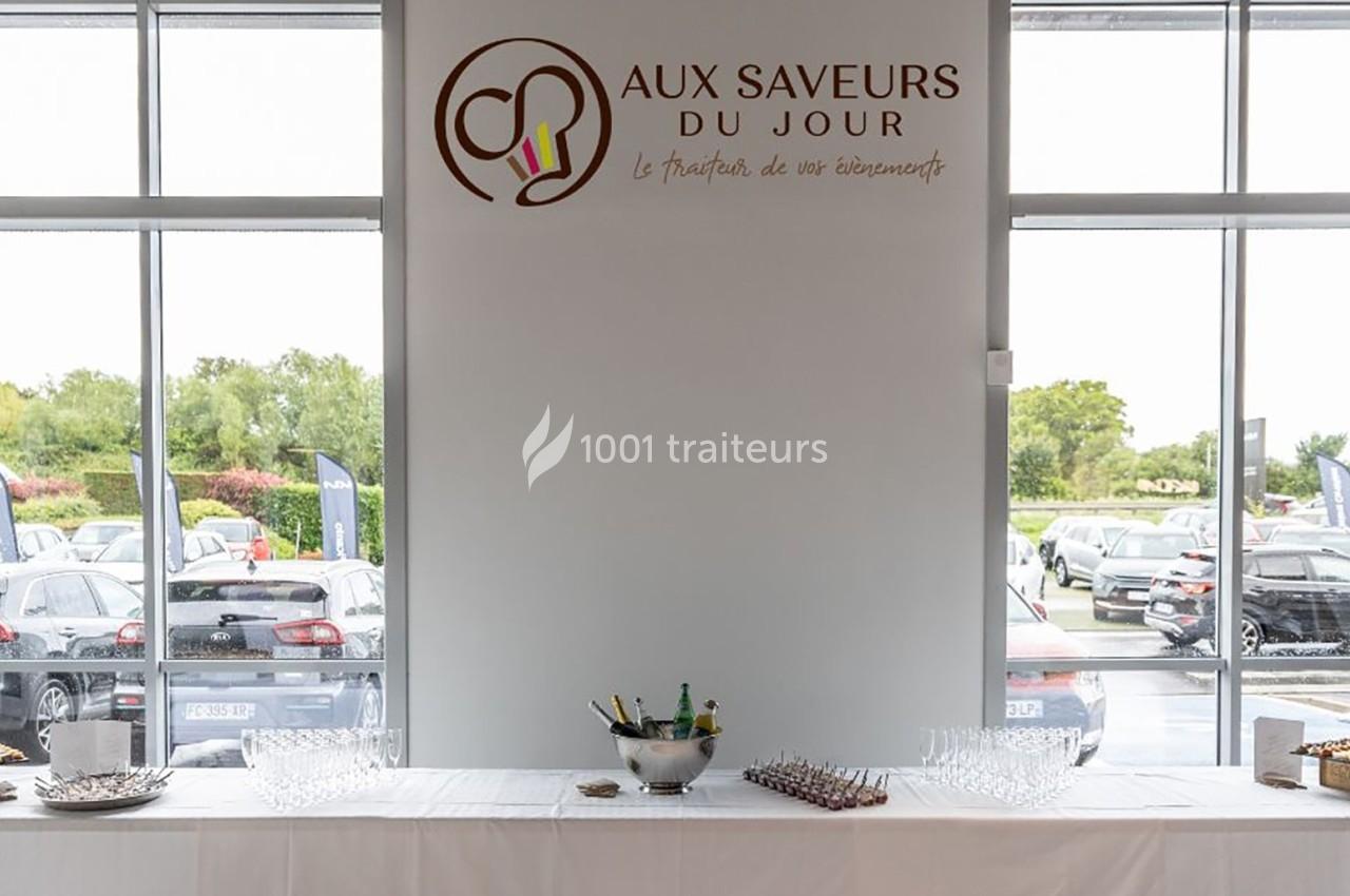 Table dressée avec des verres et un seau à champagne devant une baie vitrée, logo ’Aux Saveurs du Jour’ au mur.