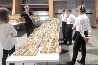 Des serveuses en tenue professionnelle observent une longue table garnie de plateaux de bouchées apéritives.