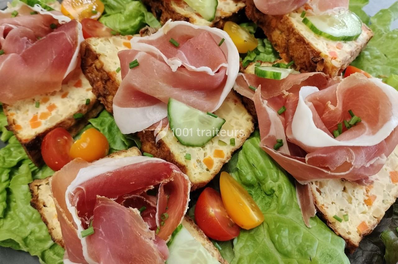 Tranches de terrine aux légumes sur lit de salade, garnies de jambon cru, tomates cerises et rondelles de concombre.