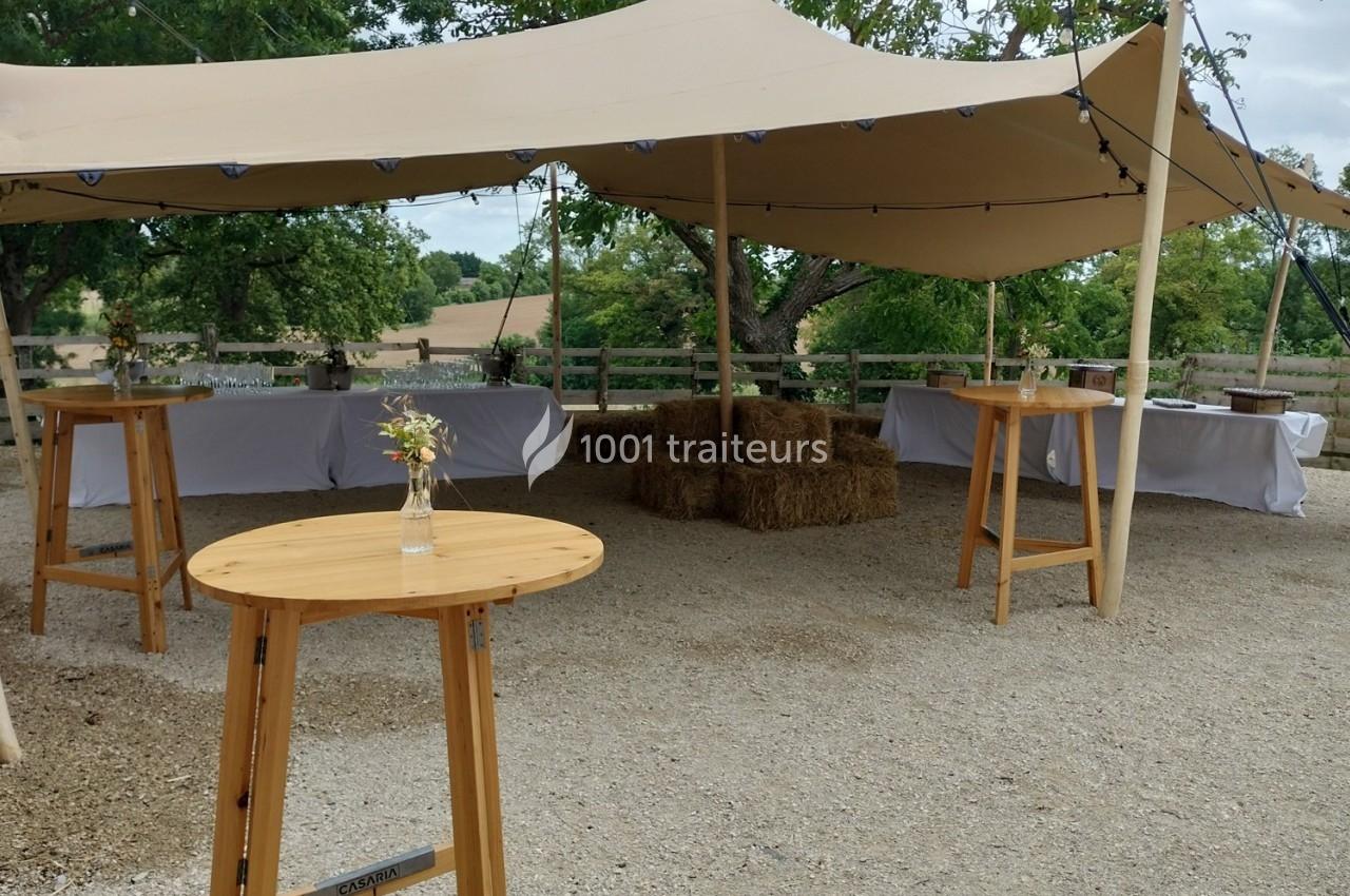Tente beige avec tables en bois, bottes de paille et tables dressées en arrière-plan dans un cadre champêtre.