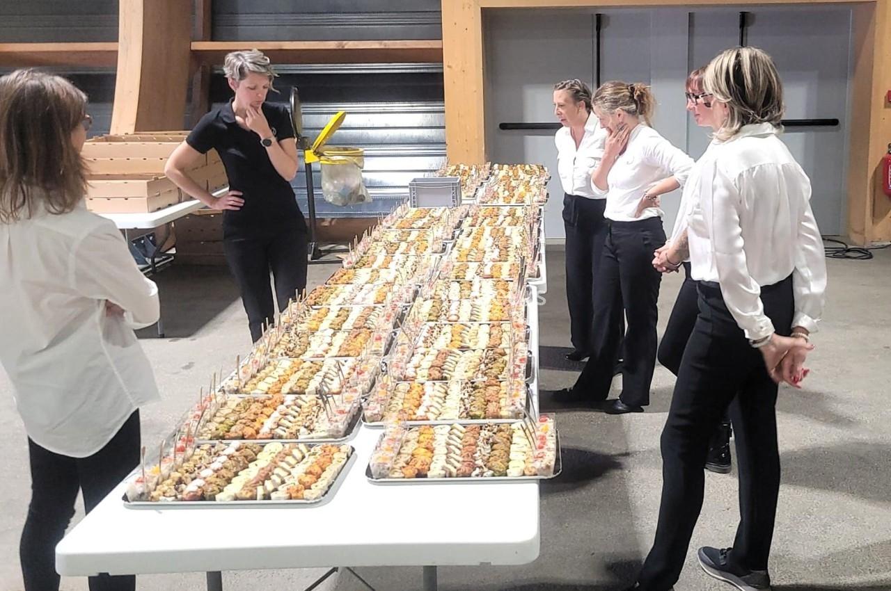 Des serveuses en tenue professionnelle observent une longue table garnie de plateaux de bouchées apéritives.