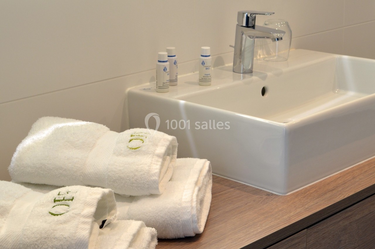 Lavabo moderne avec robinet chromé, serviettes blanches pliées et produits de toilette sur un plan en bois.