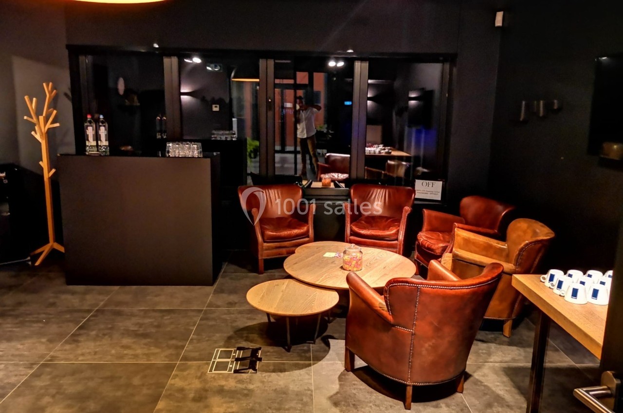 Espace lounge avec fauteuils en cuir, tables basses en bois et éclairage tamisé dans un décor sombre et moderne.