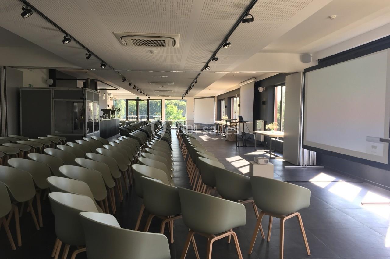 Salle de conférence lumineuse avec des rangées de chaises modernes et des écrans de projection en arrière-plan.