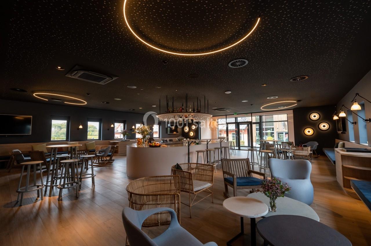 Salle moderne avec éclairage tamisé, mobilier varié et grandes fenêtres donnant sur l'extérieur.